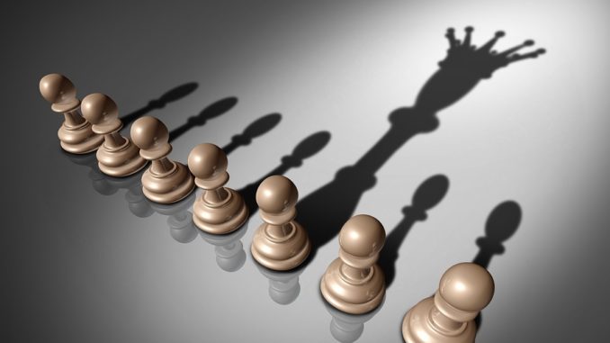 Leadership search and business recruitment concept as a group of pawn chess pieces and one individual standing out with a king crown cast shadow as a metaphor for the chosen one.